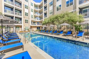 Dallas apartment for rent - A swimming pool with lounge chairs and umbrellas in front of apartment buildings.