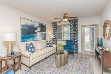 Jacksonville apartment for rent - A living room with a white couch, a blue chair, and a painting on the wall.