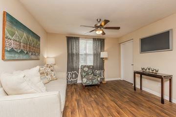 Jacksonville apartment for rent - A living room with a white couch, a painting on the wall, a ceiling fan, and a wooden table with candles on it.