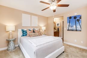 Bradenton apartment for rent - A bedroom with a large bed, a ceiling fan, and a painting of palm trees on the wall.
