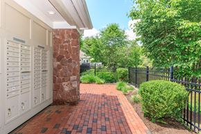 Simsbury apartment for rent - A brick pathway leads to a white building with a black fence and greenery on the side.