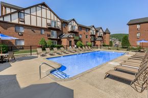 Waterbury apartment for rent - A large swimming pool surrounded by lounge chairs and umbrellas in front of a multi-story apartment building.