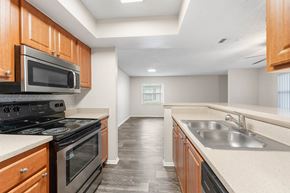 Orlando apartment for rent - A kitchen with a black stove top oven and microwave, wooden cabinets, and a sink.