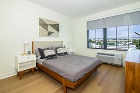 Jersey City apartment for rent - A bedroom with a bed, nightstand, and window overlooking a cityscape.