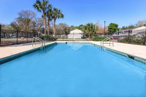 Jacsksonville apartment for rent - A swimming pool surrounded by a black fence with trees in the background.