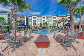 Jacksonville apartment for rent - A pool surrounded by chairs and umbrellas with apartment buildings in the background.