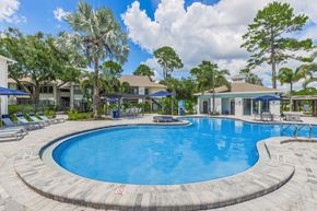 Orlando apartment for rent - A large outdoor swimming pool surrounded by trees and lounge chairs.