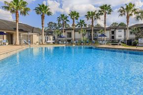 Jacksonville apartment for rent - A swimming pool surrounded by palm trees and apartment buildings.