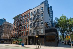 New York apartment for rent - A modern building with a glass facade is situated next to a traditional brick building with a fire escape.