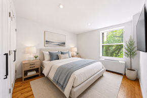 New York apartment for rent - A bedroom with a large bed and a window showing greenery outside.