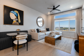 Sacramento apartment for rent - A living room with a painting of a woman, a black sofa, a white couch, a coffee table, and a view of the city.