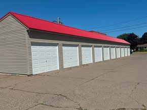 Winona apartment for rent - A building with a red roof and grey walls has four white garage doors.