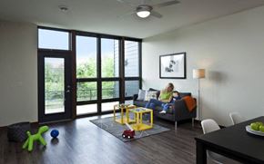 Wausau apartment for rent - A woman is sitting on a grey couch in a room with a ceiling fan and a framed picture on the wall.