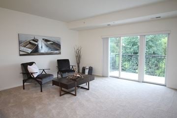 Rochester apartment for rent - A living room with a grey couch, a black chair, a coffee table, and a painting of boats on the wall.