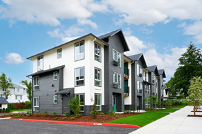 Portland apartment for rent - A modern apartment building with grey and white exterior and red mulch in the front yard.