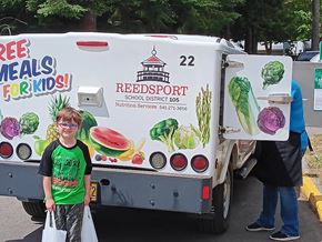 Reedsport apartment for rent - A truck with a Reedsport school district logo and a sign that says "Free Meals for Kids!" is parked in a parking lot.