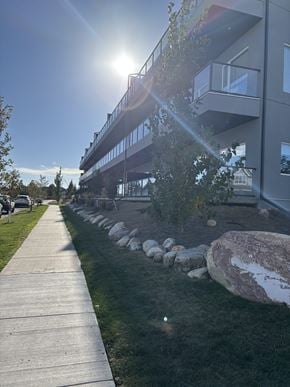 Saskatoon apartment for rent - A sunny day in front of a modern building with a walkway and a rock garden.