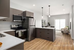 Saskatoon apartment for rent - A modern kitchen with a stainless steel refrigerator and oven, and a dining area with a table and chairs.