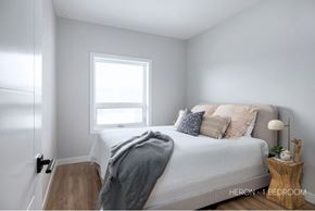 Saskatoon apartment for rent - A bedroom with a bed, a window, and a lamp on a side table.