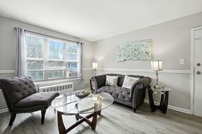 Washington apartment for rent - A living room with a grey couch, a black chair, and a glass coffee table at Huntwood Courts Apartments, Washington DC