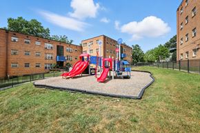 Washington apartment for rent - A playground with a red slide and a blue slide in the middle of a grassy area at Huntwood Courts Apartments, Washington DC