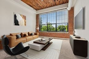Baltimore apartment for rent - A living room with a brown leather couch, a black chair, a wooden coffee table, and a flat screen TV mounted on the wall.