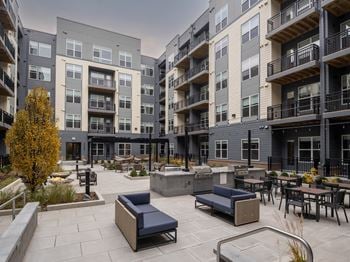 A modern outdoor seating area with benches and tables is surrounded by multi-story apartment buildings