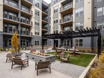 A patio with a fire pit and chairs in front of apartment buildings