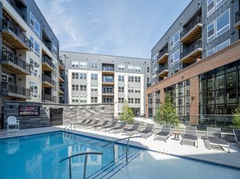 A swimming pool is surrounded by sun loungers in a sunny courtyard.