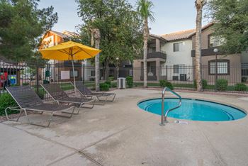 A pool area with a yellow umbrella and lounge chairs.
