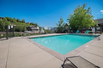 Hideout apartment for rent - A large outdoor swimming pool surrounded by a fence and lounge chairs.