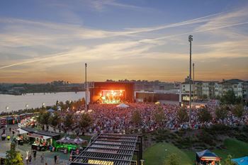 A crowd of people in front of a stage with a sunset in the background