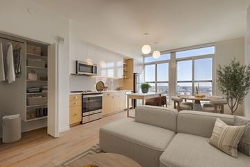 Baltimore apartment for rent - A modern living room with a grey couch and a kitchen area with wooden cabinets.