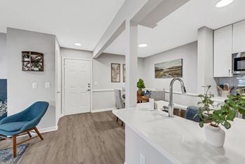 A kitchen and living room with a blue chair and white countertops