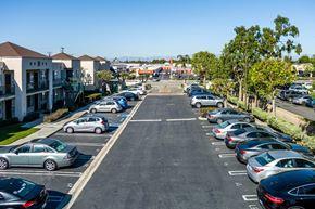 Lakewood apartment for rent - A parking lot with cars parked in rows and apartment buildings in the background. at Whispering Fountains Lakewood, Lakewood Bar, CA 90805