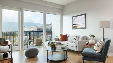 Golden apartment for rent - A living room with a grey couch, a blue chair, a grey ottoman, a coffee table, and a painting on the wall.