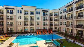 St. Louis apartment for rent - Looking at the amenity courtyard from above. The pool is below, surrounded by lounge chairs. There is outdoor couches and a game area just below to the right. The apartment building surrounds the scene.