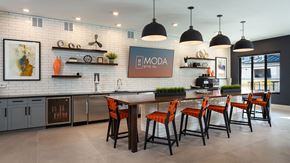 St. Louis apartment for rent - The catering kitchen at Moda at The Hill. A large bar sits in front of the kitchen that runs along the back wall. There are shelves with knick-knacks on them and a large screen television.