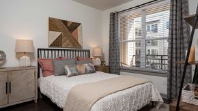 St. Louis apartment for rent - A residence bedroom with a large bed set nicely in the middle, a night stand on both sides. The balcony is seen outside the window.