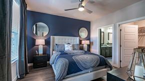 Phoenix apartment for rent - A modern bedroom with a navy blue accent wall, white tufted headboard, and matching blue bedding. two round mirrors hang above bedside tables, and an open door leads to a bathroom.