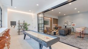 Aurora apartment for rent - Modern resident entertainment lounge at Tempo at Nine Mile featuring a shuffleboard table, lounge seating, coworking space, and contemporary interior design.