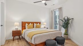 Aurora apartment for rent - Modern apartment bedroom with wood bed frame, neutral bedding, bedside lamps, wood-style flooring, and large window with natural light.