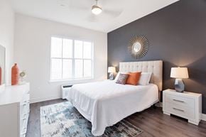 Kearny apartment for rent - A bedroom with a white bed and a white nightstand with a lamp on it.