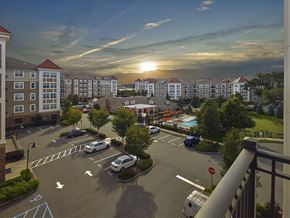 Lyndhurst apartment for rent - A sunset view of a parking lot with cars parked and a pool in the distance at Vermella Lyndhurst apartments, Lyndhurst, New Jersey