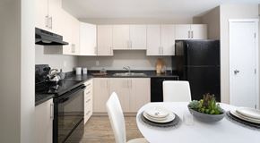 Winnipeg apartment for rent - A modern kitchen with black countertops and light cabinets, black appliances. a kitchen table set of four sits in the center