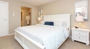 Campbell River apartment for rent - A white bedroom with a large bed, nightstand, and a painting on the wall.