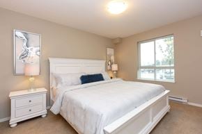 North Cowichan apartment for rent - A bedroom with a white bed and a white nightstand with a lamp on it.