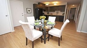 Edmonton apartment for rent - A warm lit kitchen with dark cabinets, light counter tops and black appliances, a large open space with a kitchen table set for four