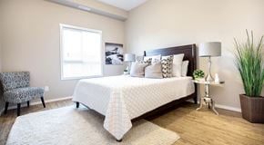 Winnipeg apartment for rent - A bedroom with queen sized bed, night stands and a chair. A large window with blinds on far wall.