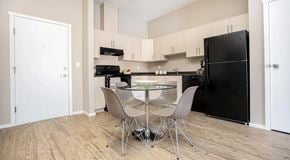 Winnipeg apartment for rent - An open kitchen, with light cabinets, dark counters and black appliances. A round table with four chairs around it sits in the centre